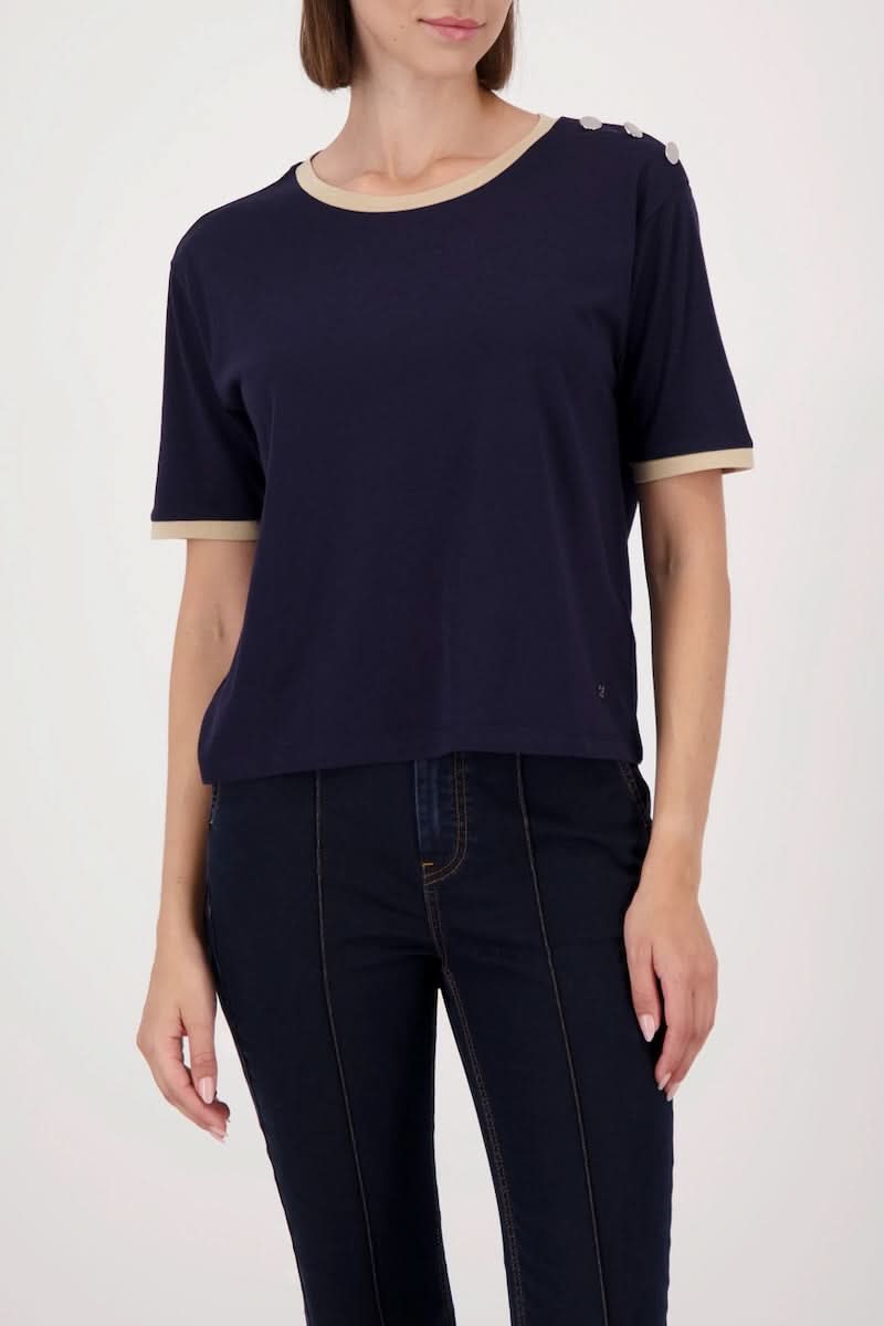 Femme portant un T-shirt à boutons décoratifs sur l’épaule, finitions contrastantes, look décontracté chic.