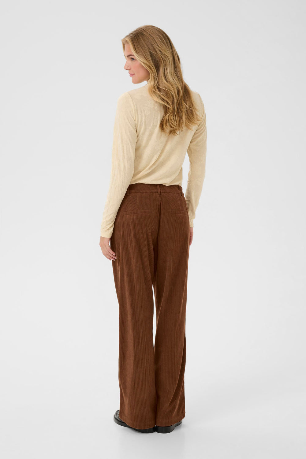 Femme portant un Pantalon Kanna en velours côtelé à jambe large. Vue de dos du pantalon brun en velours côtelé, style élégant et moderne.