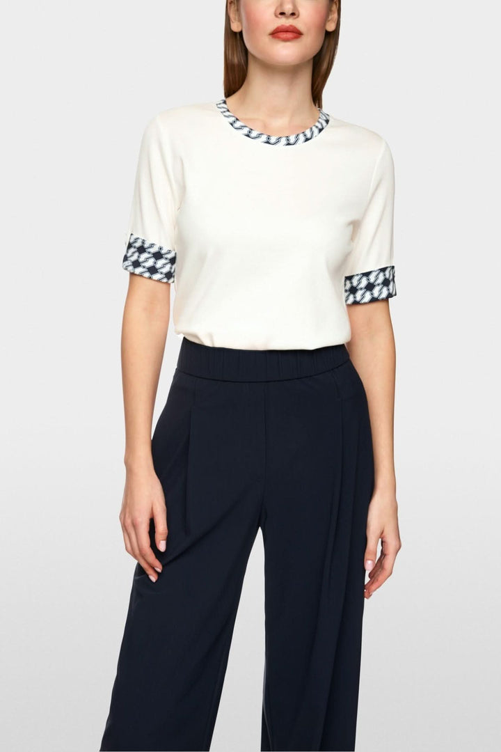 T-shirt en jersey blanc avec encolure ronde et manches mi-longues à motifs géométriques, porté avec un pantalon noir.