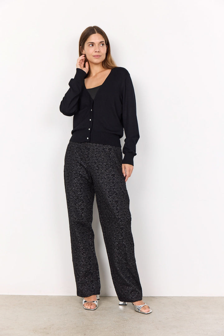Femme portant un cardigan classique noir à encolure en V avec pantalon à motifs, élégance décontractée.