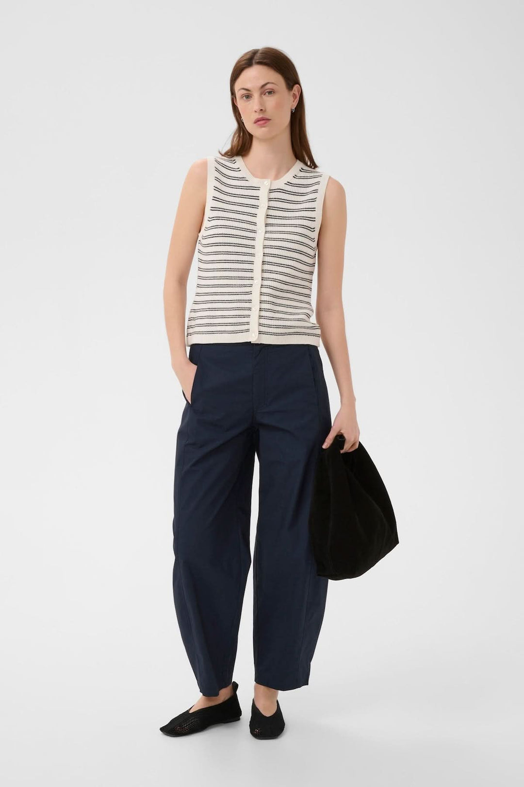 Modèle portant un Pantalon Atimas large avec poches latérales et fermeture discrète, associé à un haut rayé et des chaussures noires.