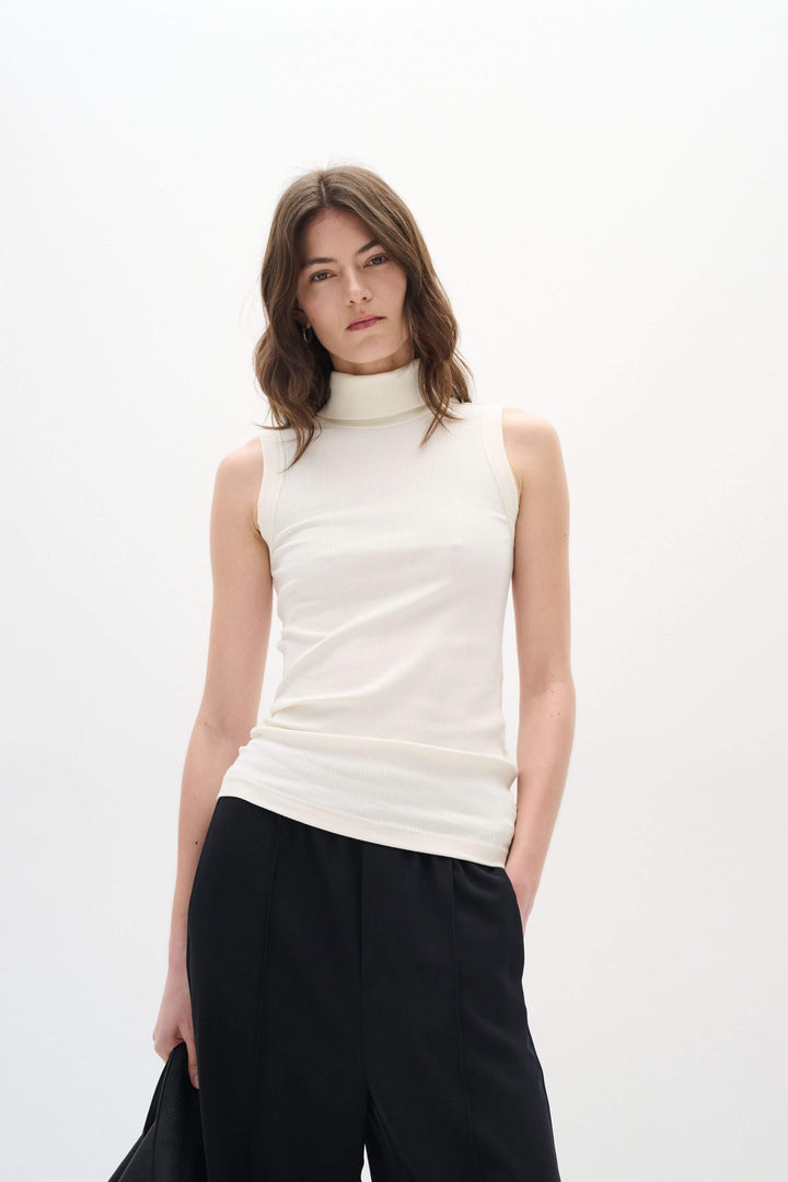 Camisole Dagna sans manches à col montant, tissu côtelé, couleur crème, style ajusté, portée avec un pantalon noir.