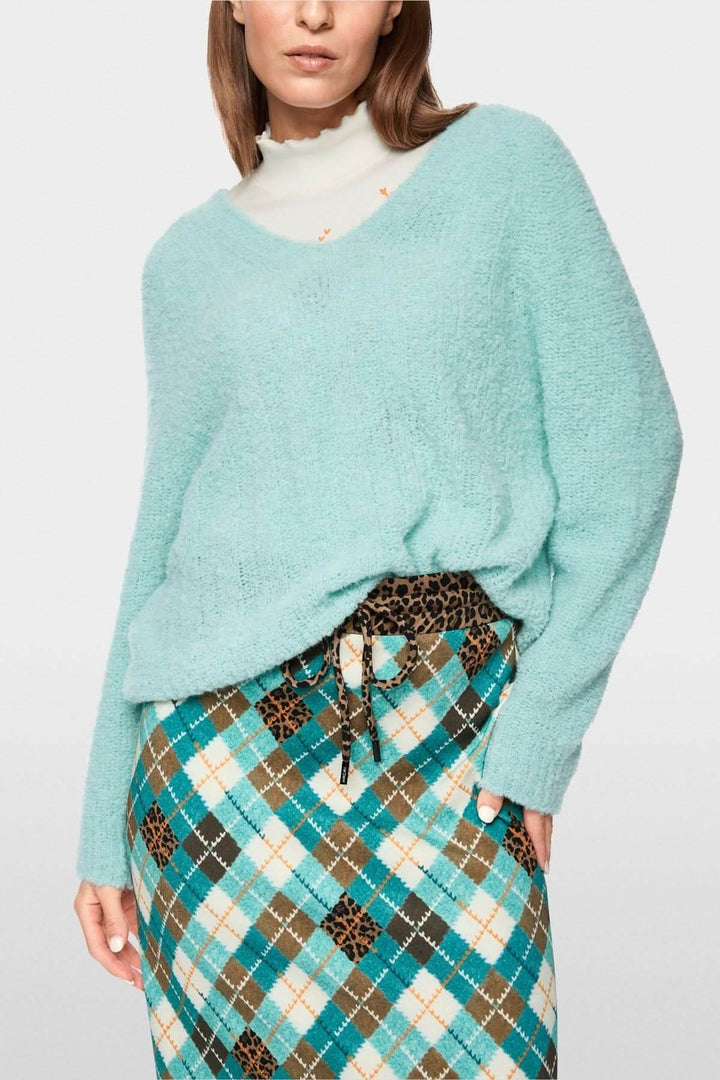 Femme portant un chandail tricoté à col en V bleu doux avec une jupe à motif. Chandail confortable et élégant pour la mi-saison.