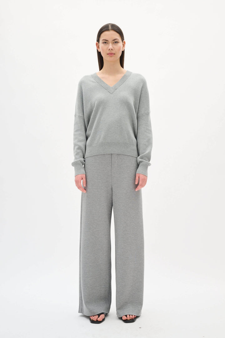 Chandail col en V en coton gris, coupe décontractée, porté avec un pantalon assorti, look moderne et confortable.