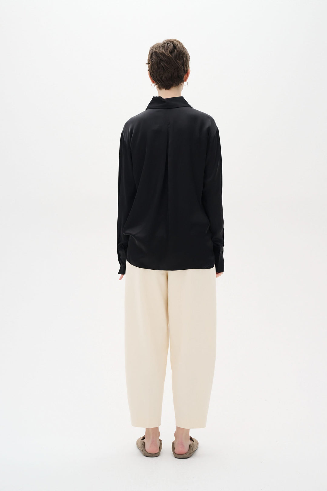 Chemise Pauline satinée noire vue de dos, portée avec un pantalon ample beige, offrant un style chic décontracté.