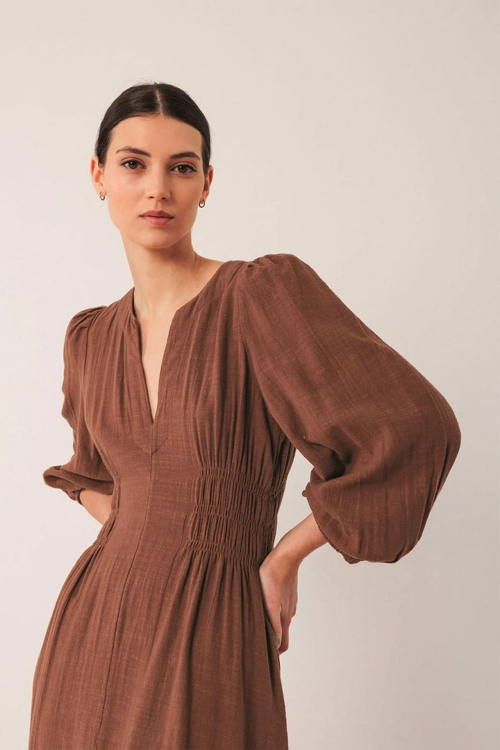 Femme portant une robe longue à encolure V et manches bouffantes, mise en valeur par des smocks à la taille pour un look chic.