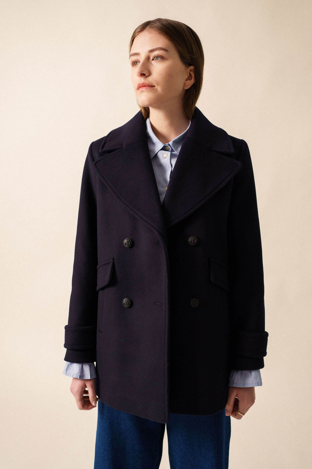 Manteau chic noir à col large, fermeture à double boutonnage, porté sur une chemise.