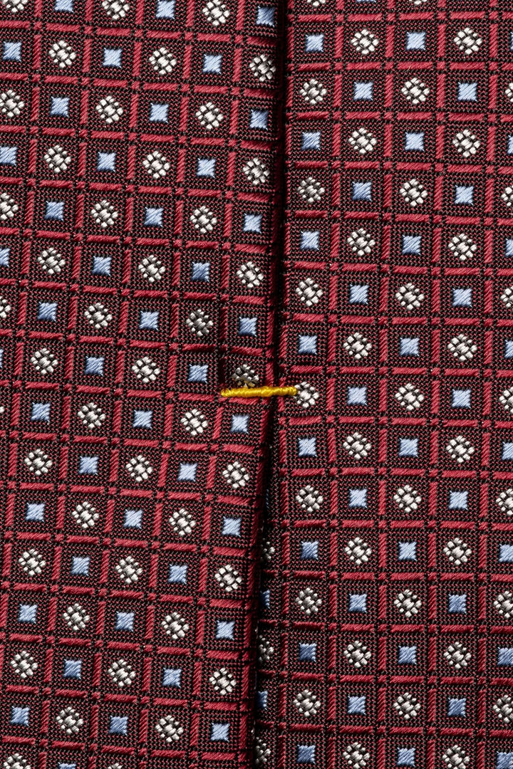 Cravate motif géométrique en rouge et bleu, texture satinée avec détails raffinés, idéale pour une tenue formelle.