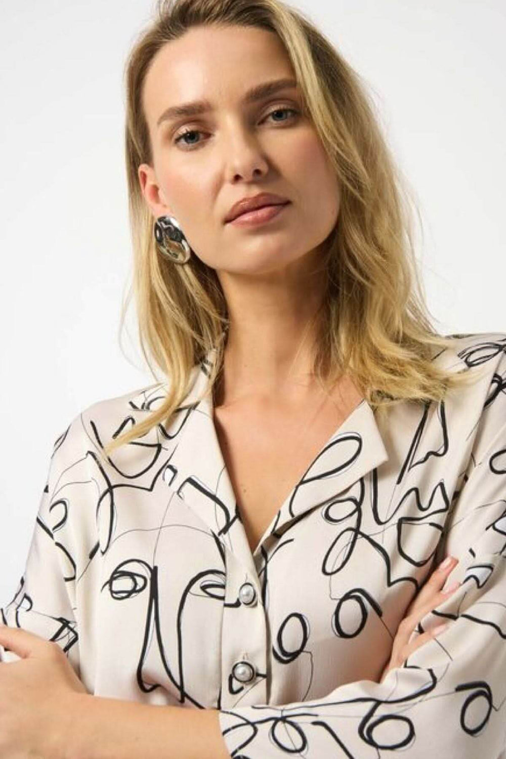 Blouse imprimée graphique avec col chemise et motifs abstraits de visages, style moderne et artistique.