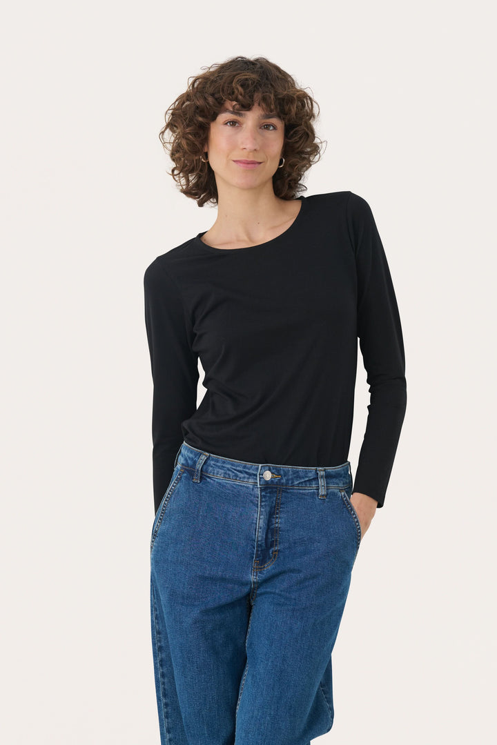 Femme portant un chandail à manches longues noir en jersey extensible avec jeans, style décontracté et élégant.