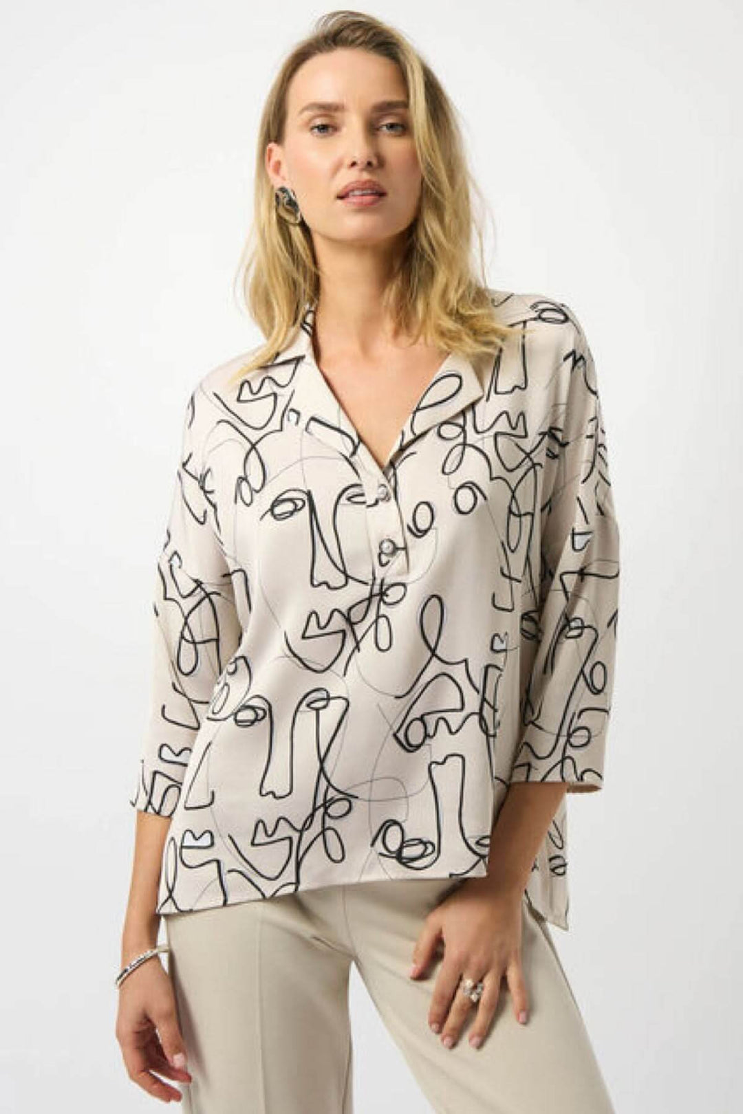 Blouse imprimée graphique avec motifs abstraits de visages, col chemise et manches mi-longues, style moderne et élégant.