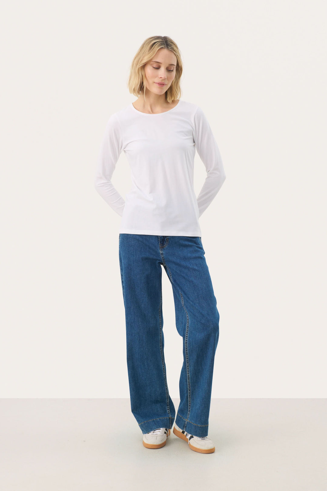 Femme portant un chandail à manches longues blanc et un pantalon denim large, style décontracté.