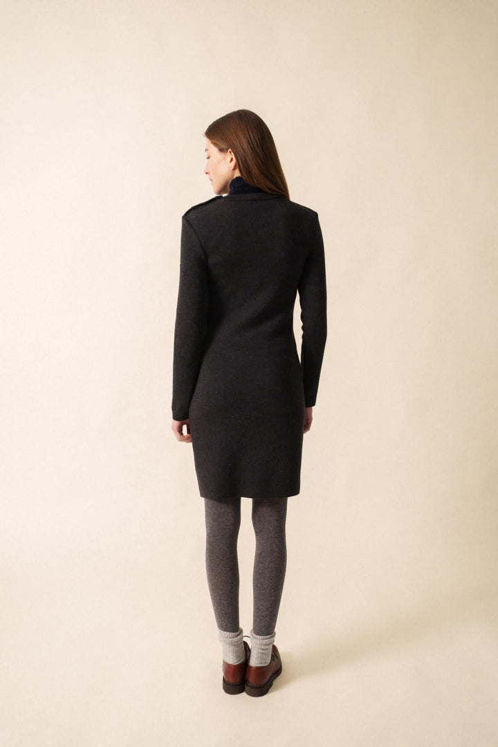 Femme de dos portant une robe ajustée en maille fine, avec collants et bottines, sur fond neutre.