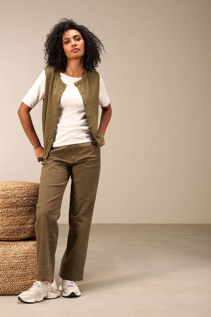 Femme en tenue minimaliste avec chandail blanc et pantalon olive, style moderne et décontracté.