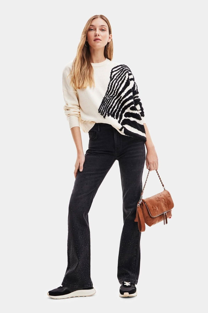 Femme portant un pull avec motif zèbre, jean noir large et sac à main en cuir, style décontracté.