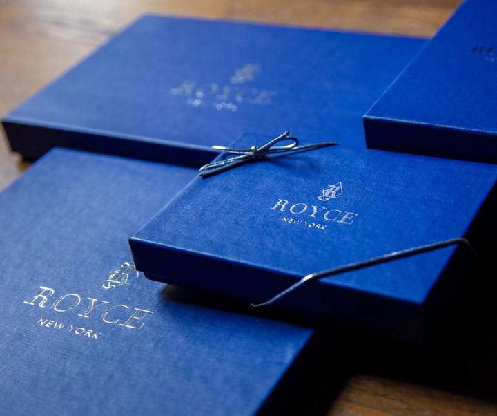 Blue luxury gift boxes from Royce New York, featuring elegant logo and stylish ribbon detail on wooden background.